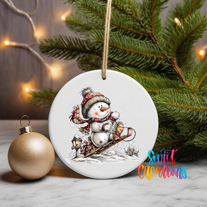 Snowman on a Sled ornament UV DTF transfer on a hanging ornament with pine branches and a gold bauble