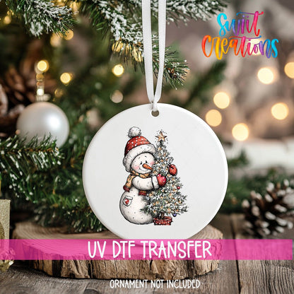 Snowman with Christmas Tree ornament UV DTF transfer on an ornament resting on a wood slice beside a Christmas tree
