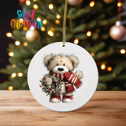 Teddy Bear with Holly Wreath ornament UV DTF transfer on an ornament on a wooden table with tree lights behind it