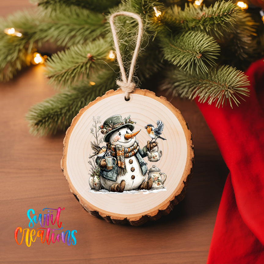 A wooden ornament featuring a snowman with a bird perched on its shoulder, surrounded by pine branches and other holiday decorations, hangs on a Christmas tree.