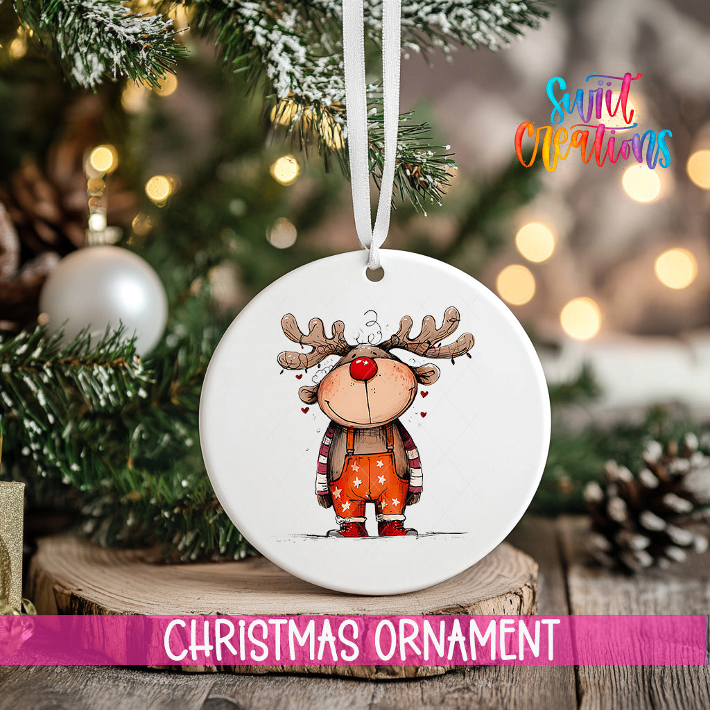 A white Christmas ornament featuring a cartoon reindeer is hanging on a tree, with a blurred background of lights and pine branches.