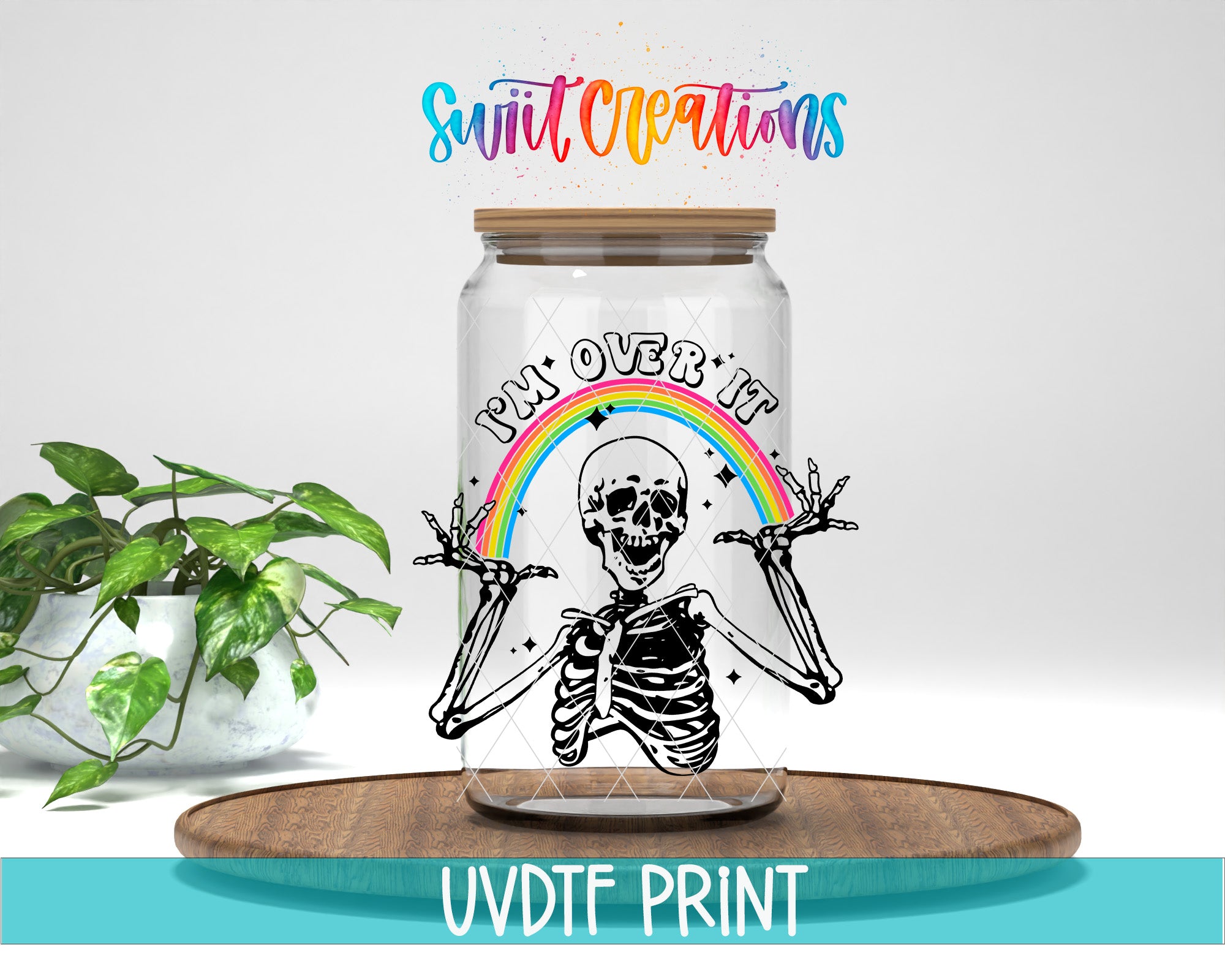 a skeleton wearing a rainbow hat and holding a rainbow-colored sign that says "I'm over it". The skeleton is inside a glass jar, which is placed on a wooden surface. There is a potted plant in the background, and the image includes text that reads "Swit Creations" and "UVDF PRINT".