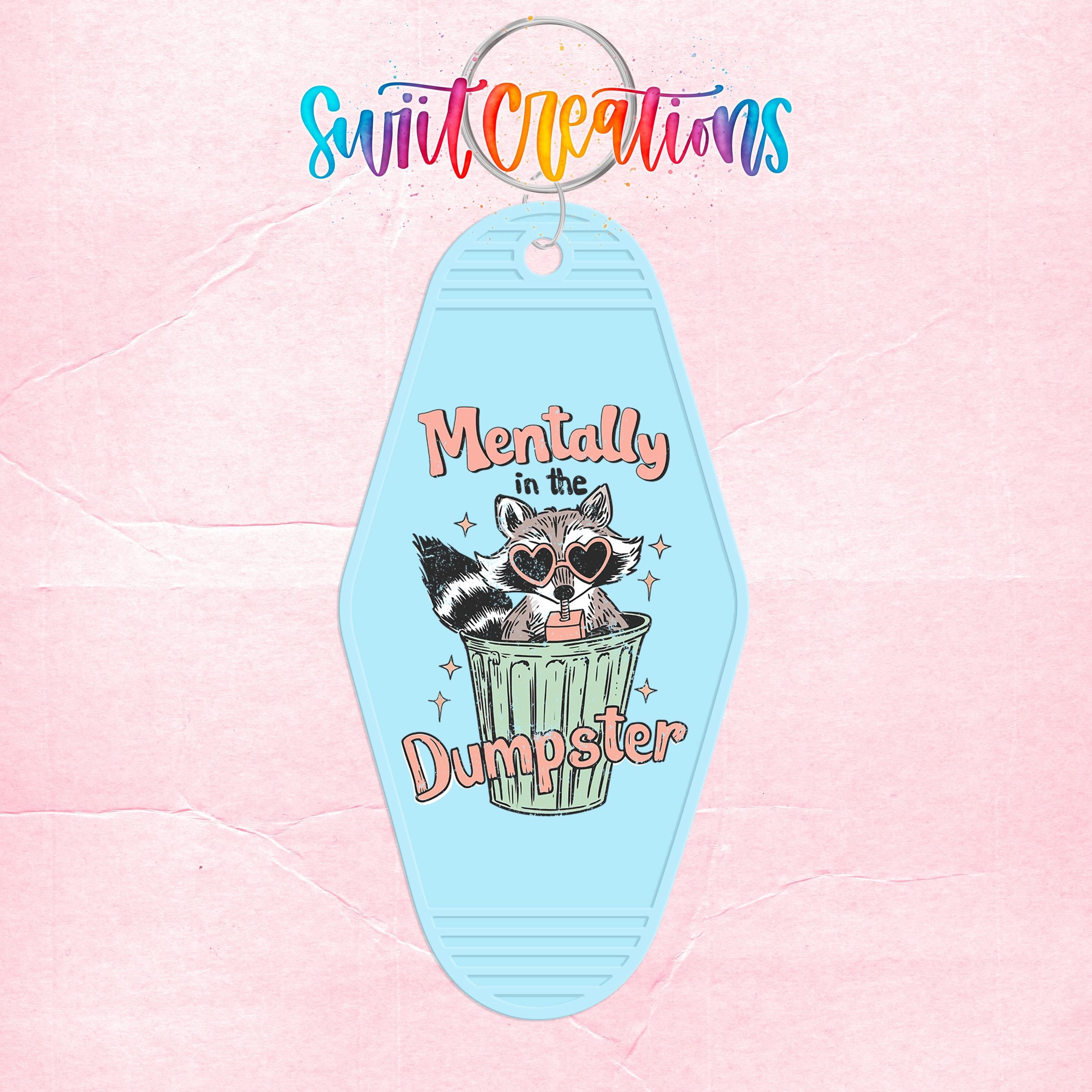 A keychain with a cartoon raccoon sitting in a trash can and the text "Mentally in the Dumpster" printed on it.