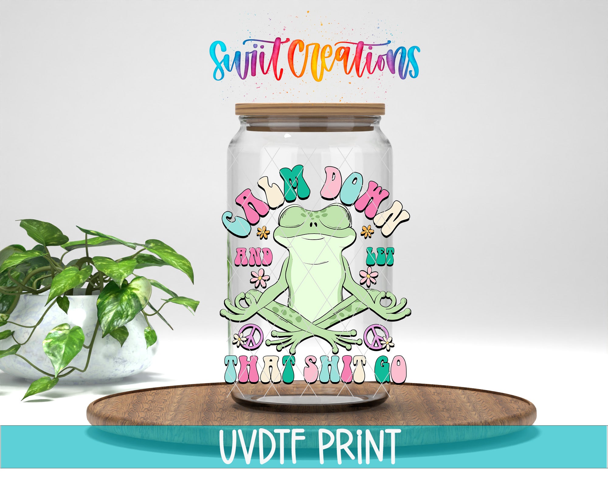 A glass jar with a frog illustration and the text "Calm down and let go" on it, placed on a wooden surface next to a potted plant.