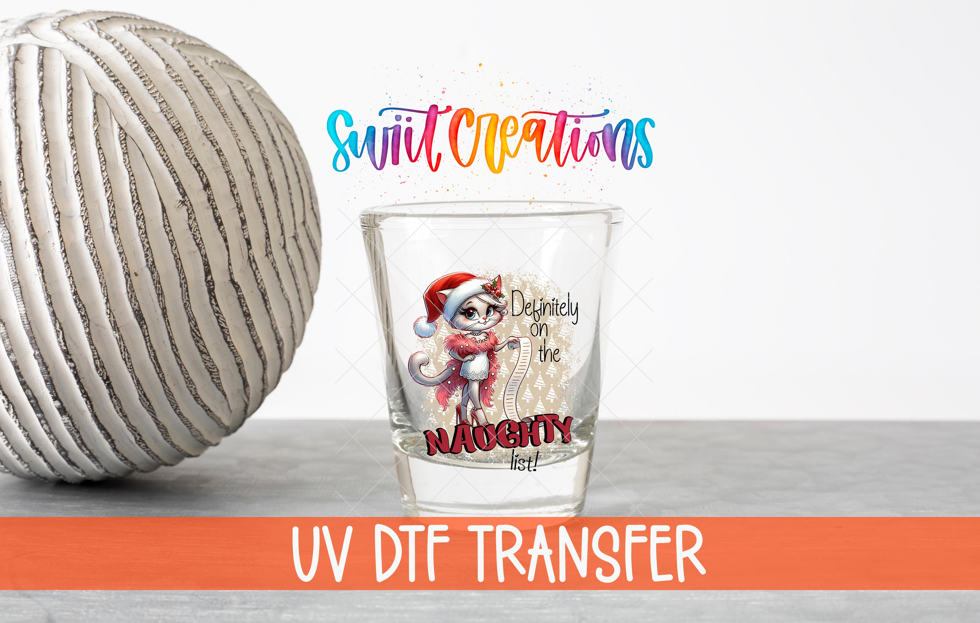a glass with a cartoon character and text, placed next to a white ball on a gray surface.