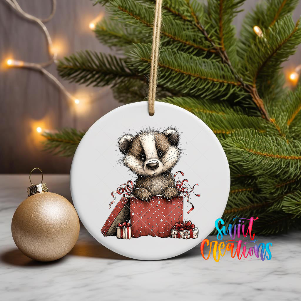 A ceramic ornament featuring a cartoon badger sitting inside a gift box, surrounded by Christmas decorations and a gold ornament on a table.