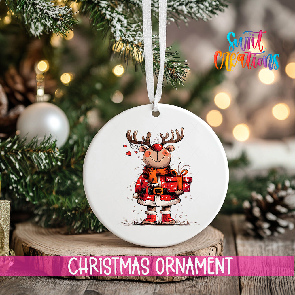 A white Christmas ornament featuring a cartoon reindeer holding a gift, hanging on a tree branch with a ribbon.