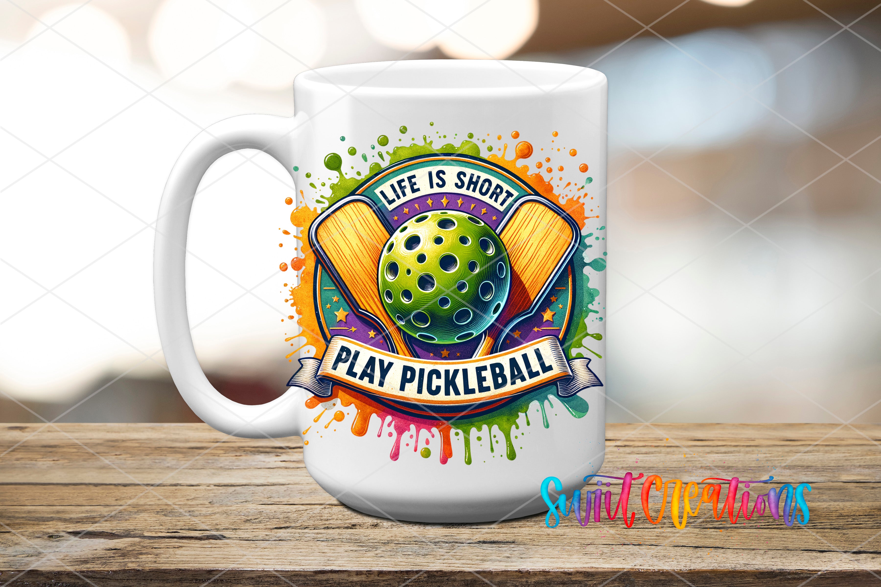 A white mug with a colorful graphic design featuring a green pickleball and the text "Life is short, play pickleball" against a background of splattered paint.