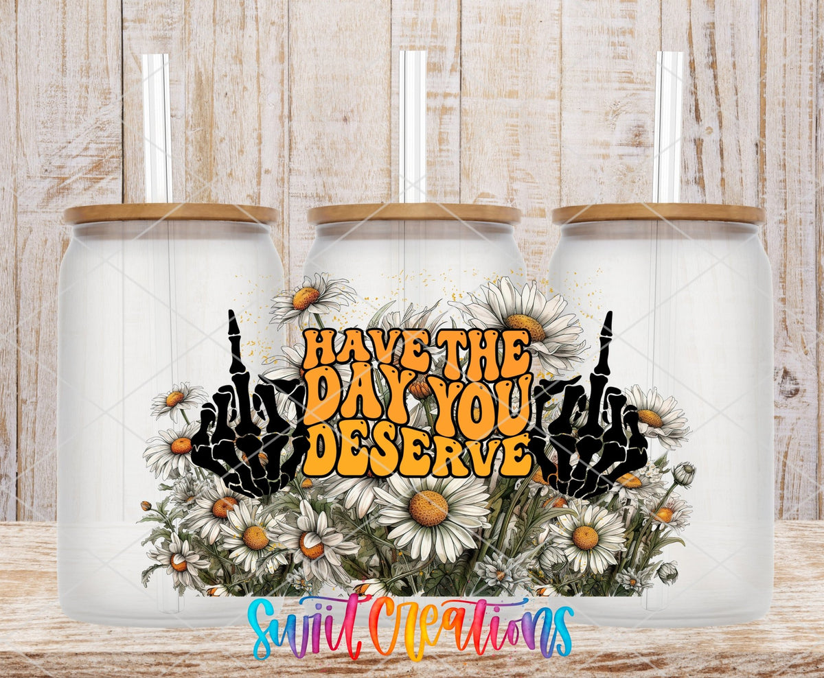 Have the Day You Deserve skeleton hands and daisies UV DTF wrap on three clear glass cans with bamboo lids
