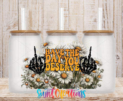Have the Day You Deserve skeleton hands and daisies UV DTF wrap on three clear glass cans with bamboo lids