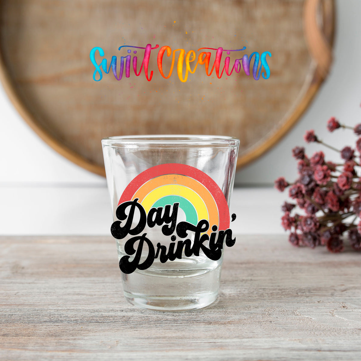 Day Drinkin' shot glass transfer on a clear glass beside a wooden barrel and dried flowers