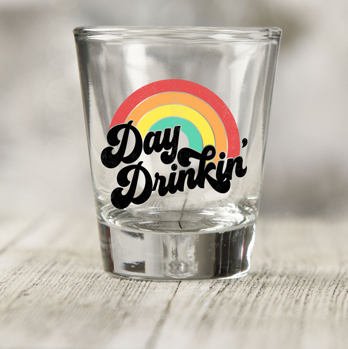 Day Drinkin' shot glass UV DTF transfer with retro rainbow graphic on a clear shot glass