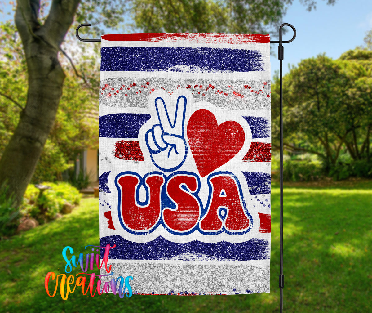 A patriotic flag with the word "USA" prominently displayed, featuring a peace sign and a red heart symbol. The flag is hanging outdoors in a grassy area with trees in the background.
