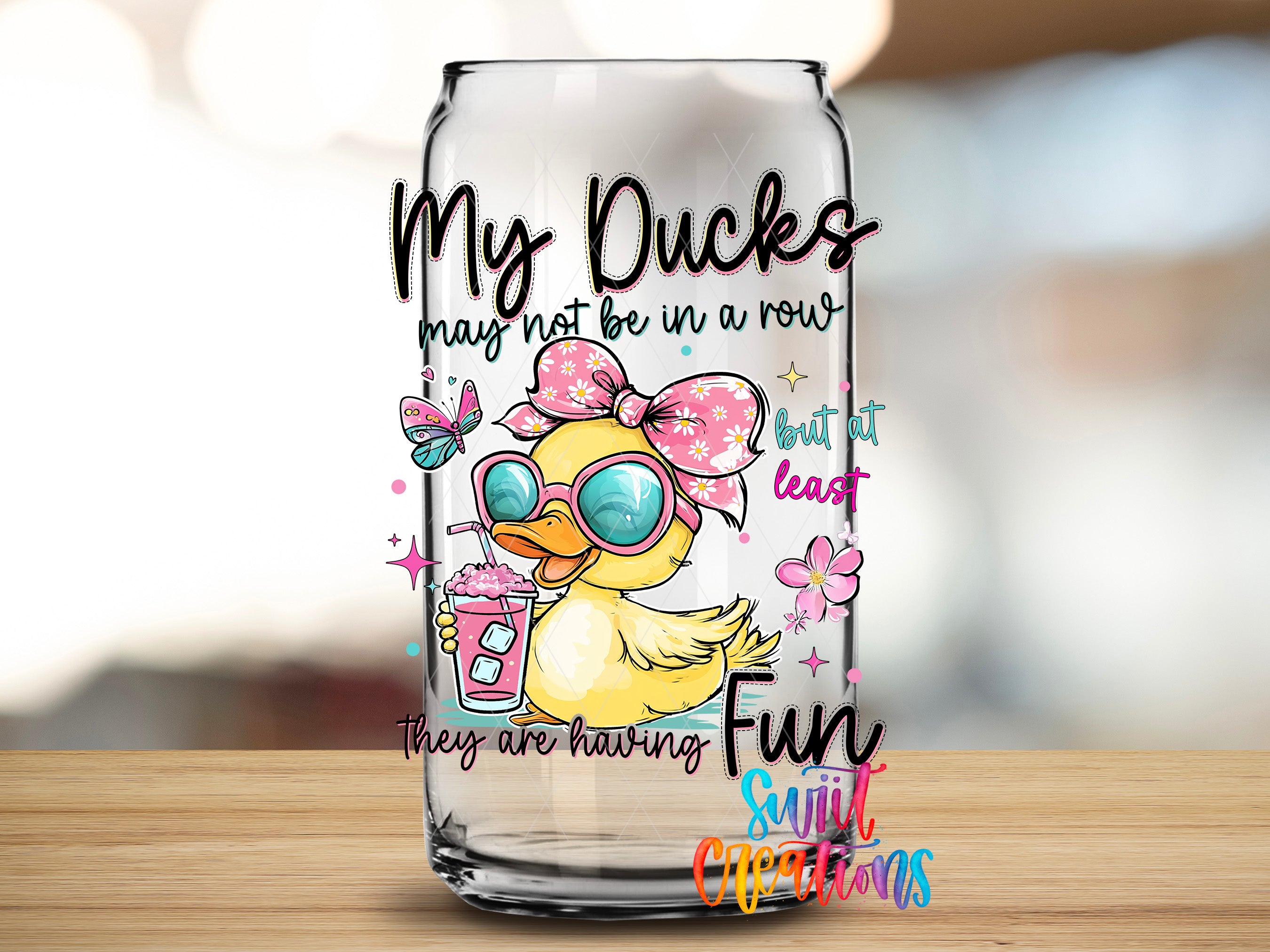 A glass can with a cartoon duck wearing sunglasses and holding a drink, along with text that reads "My Ducks may not be in a row, but at least they are having fun".