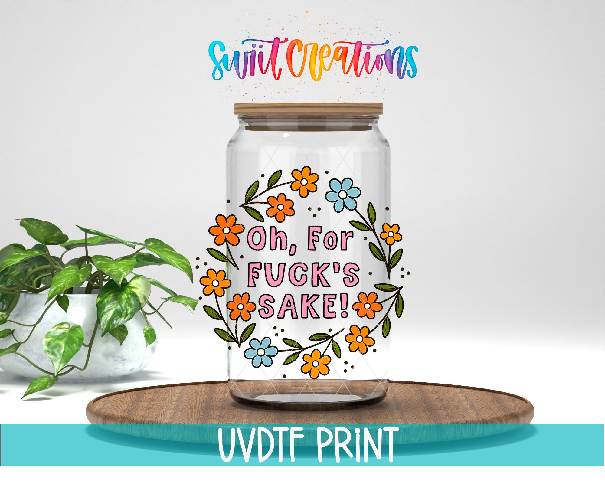 A glass jar with a floral design and text on it, placed on a wooden surface next to a potted plant.