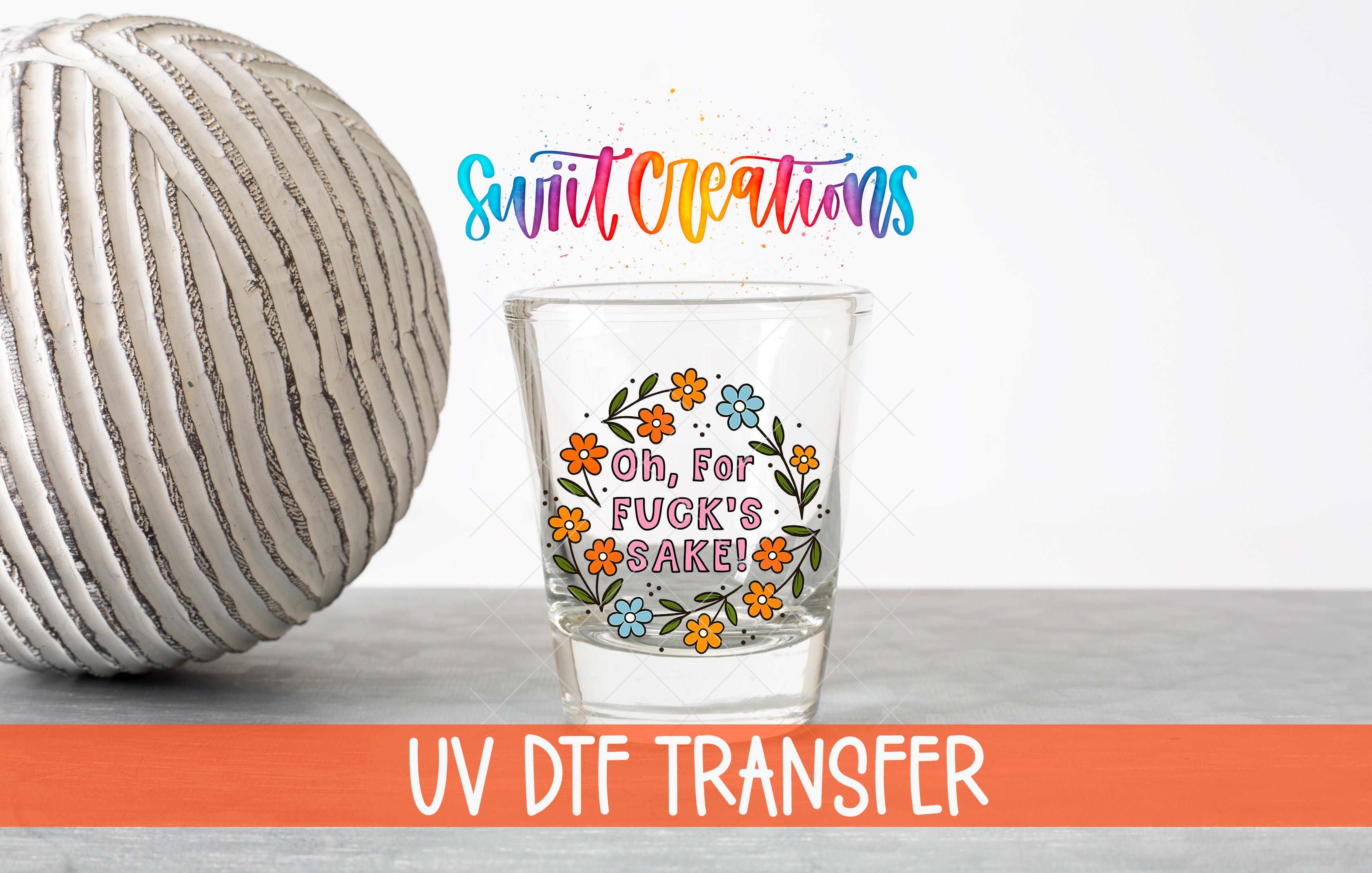 a glass with a colorful design and text, placed next to a white ball on a gray surface.