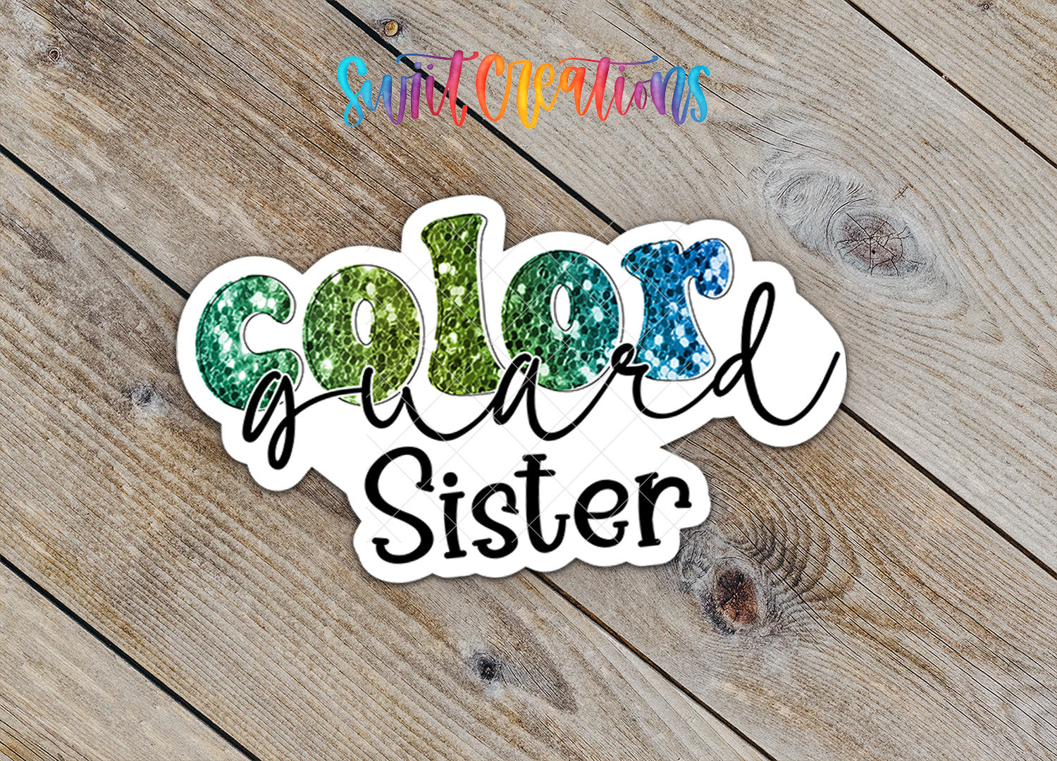 A sticker with the text "Color guard Sister" written in a colorful, glittery font, placed on a wooden surface.