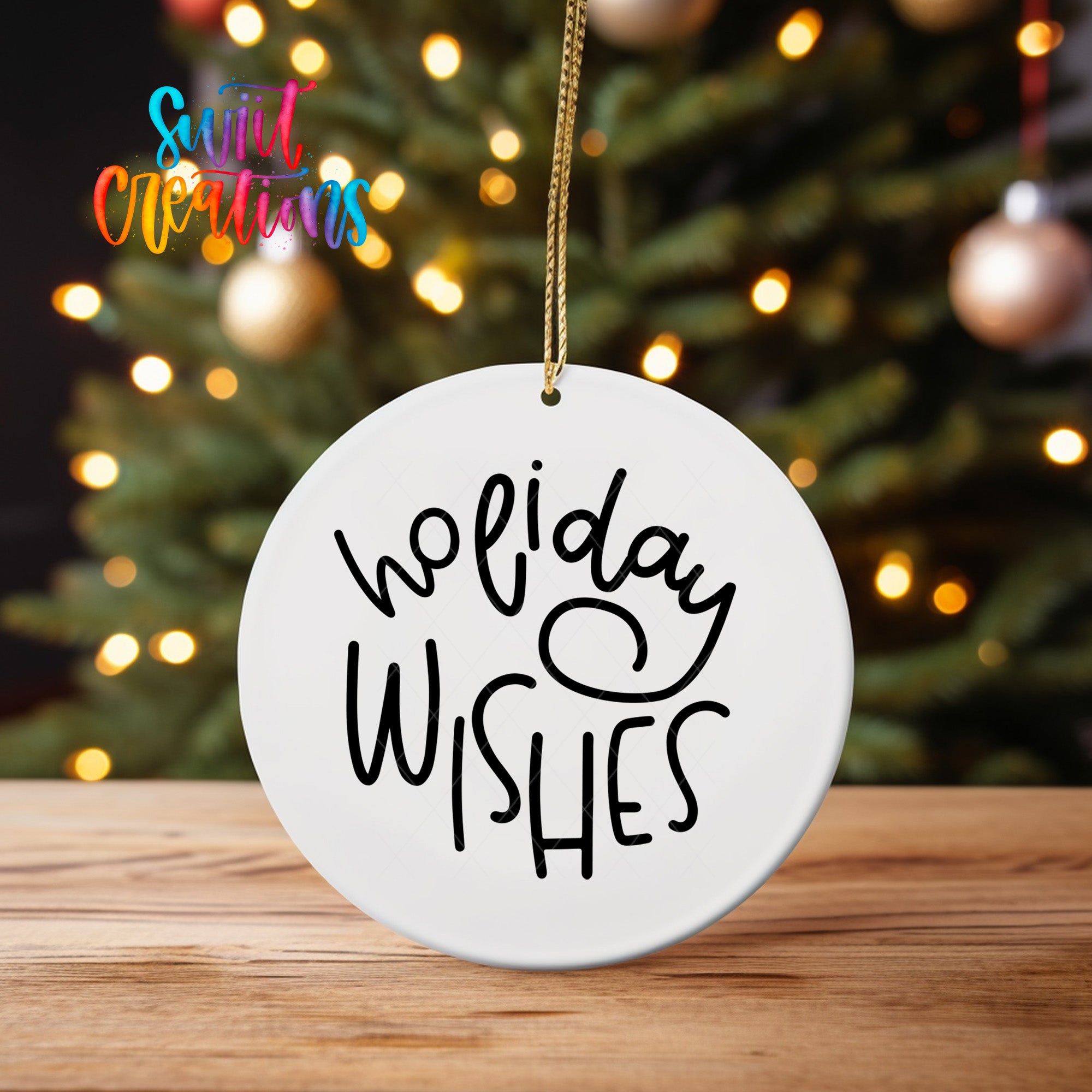 A white ornament with the text "Holiday Wishes" hanging from a string, placed in front of a blurred Christmas tree with colorful lights.