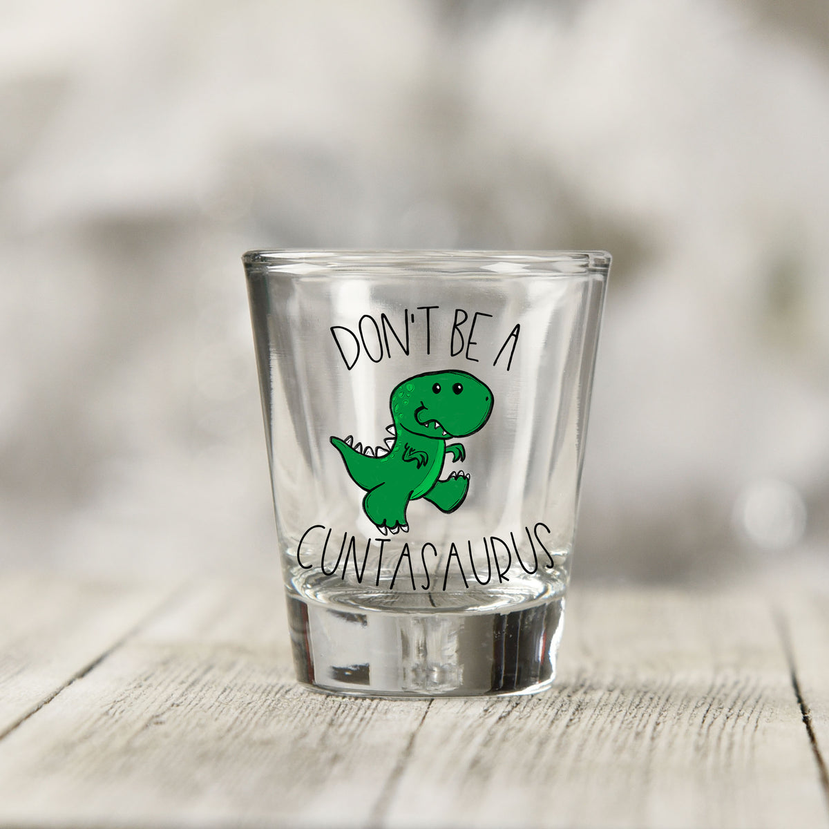 Close-up of the Don't Be a Cuntasaurus UV DTF transfer on a clear shot glass
