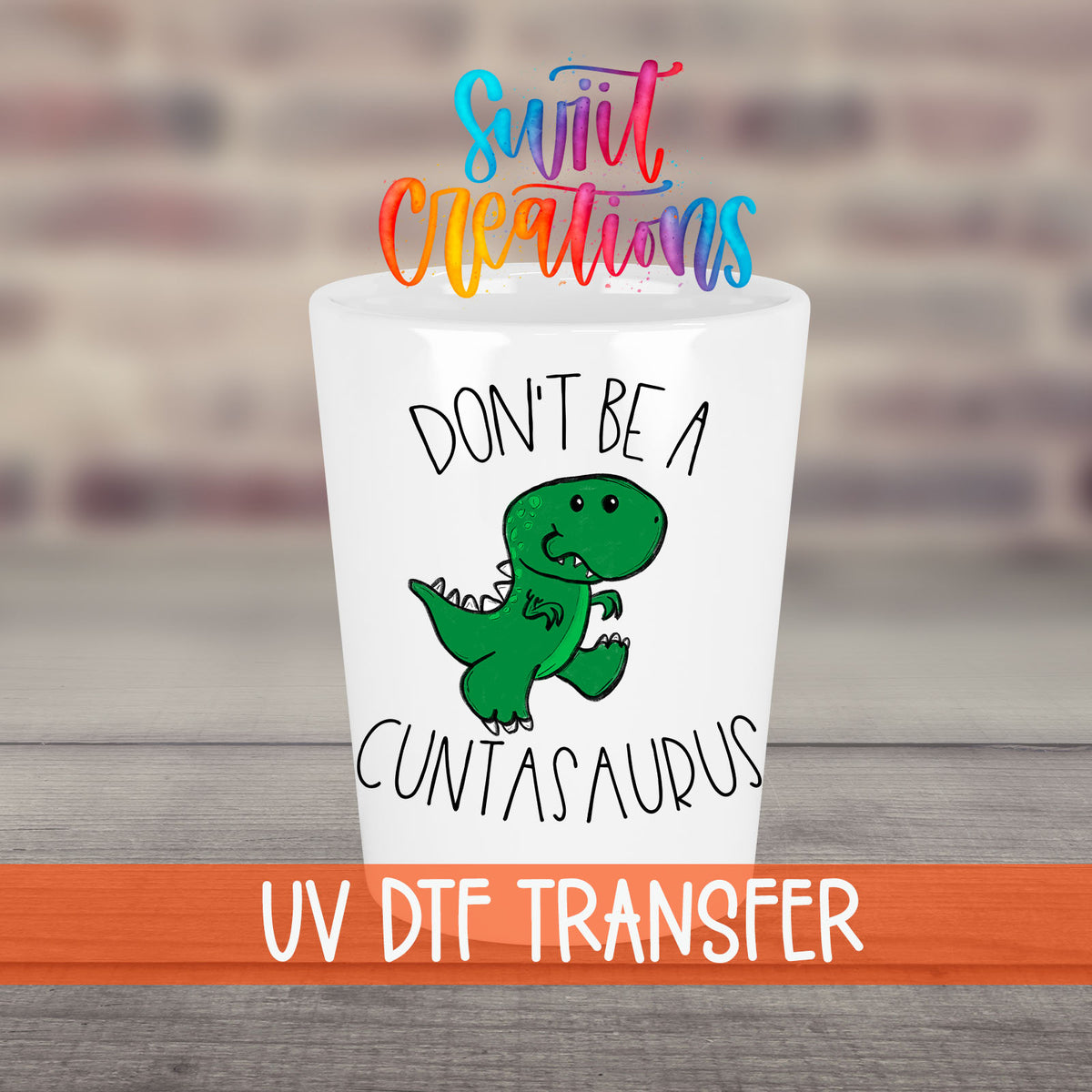 Don't Be a Cuntasaurus UV DTF transfer on a white shot glass in front of a brick wall