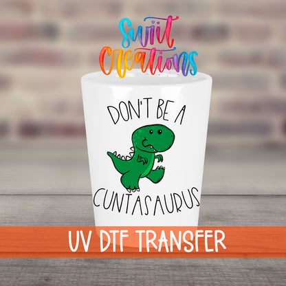 Don't Be a Cuntasaurus UV DTF transfer on a white shot glass in front of a brick wall