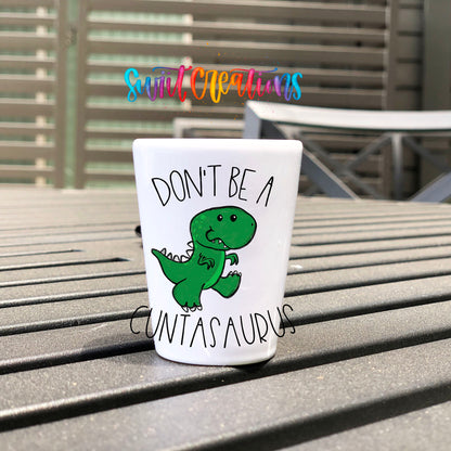 Don't Be a Cuntasaurus UV DTF transfer on a white shot glass on an outdoor patio table