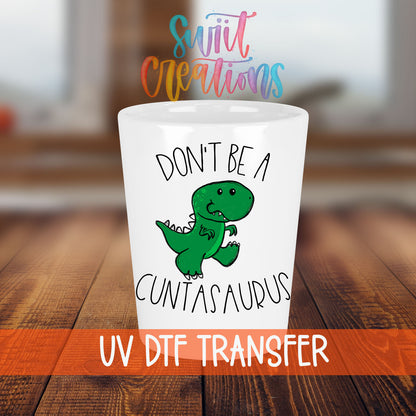 Don't Be a Cuntasaurus shot glass transfer on a white shot glass on a wooden table