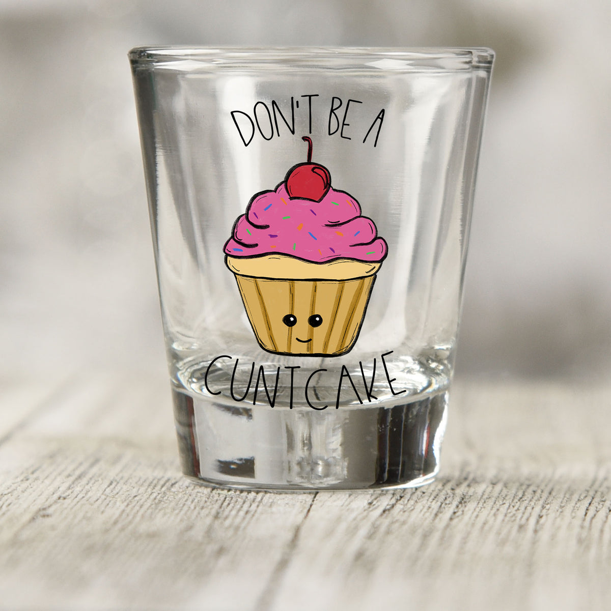 Don't Be a Cuntcake shot glass UV DTF transfer with smiling cupcake with pink frosting and a cherry on a clear shot glass
