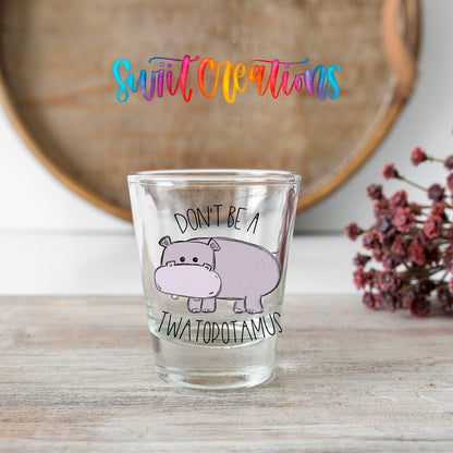 Don't Be a Twatopotamus shot glass transfer on a clear glass beside a wooden barrel and dried flowers