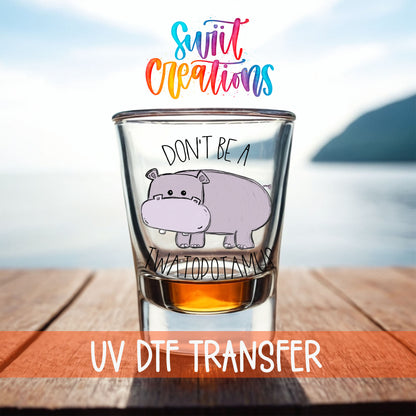 Don't Be a Twatopotamus shot glass UV DTF transfer on a filled shot glass on a dock by the water
