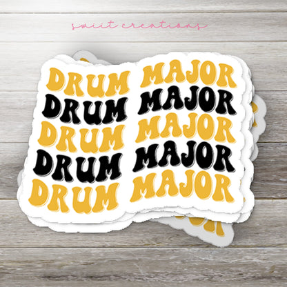 Stack of Black and Gold Drum Major glossy stickers on a gray wood table