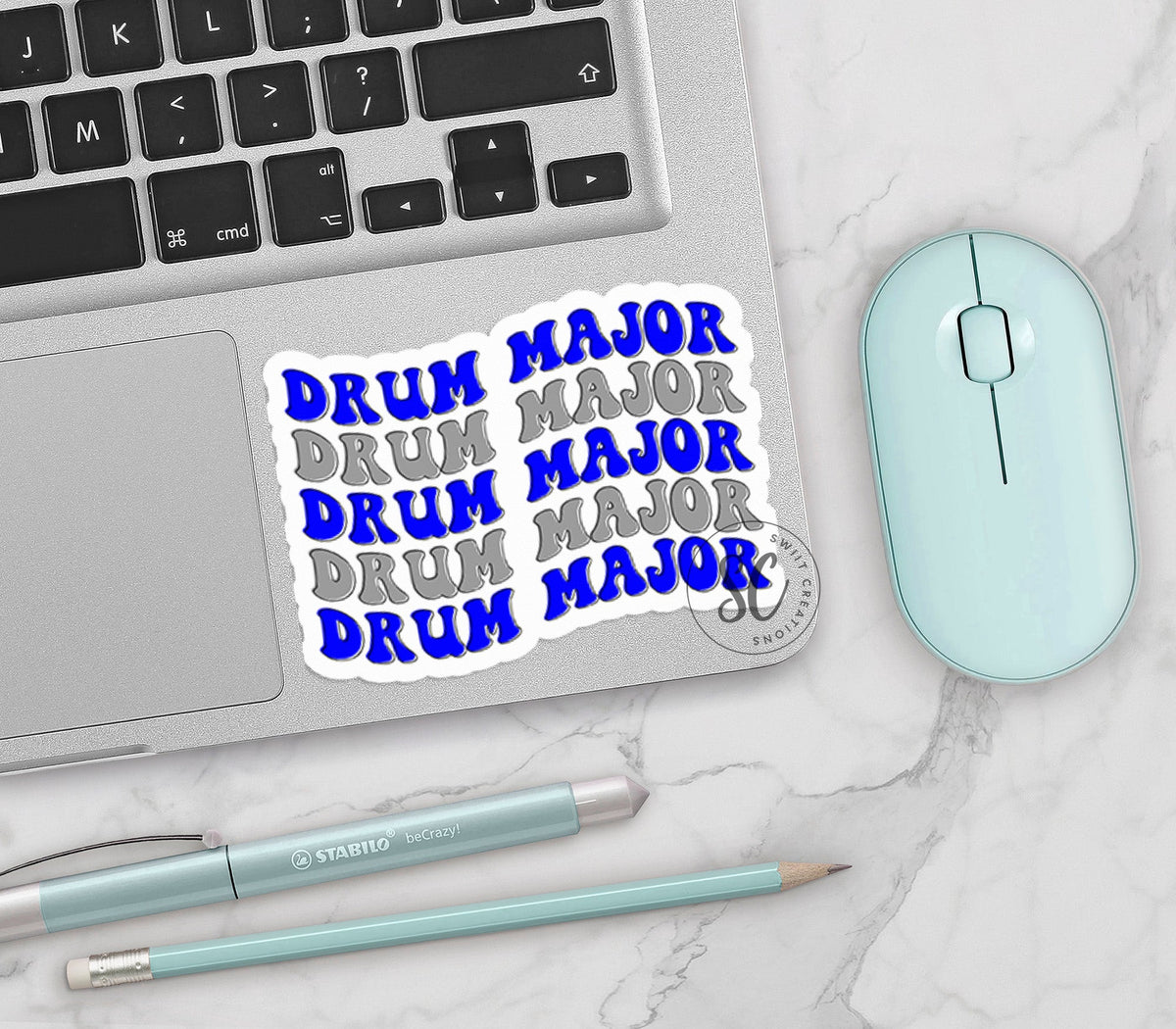 Blue and Silver Drum Major vinyl sticker on a silver laptop next to a mint mouse and pens