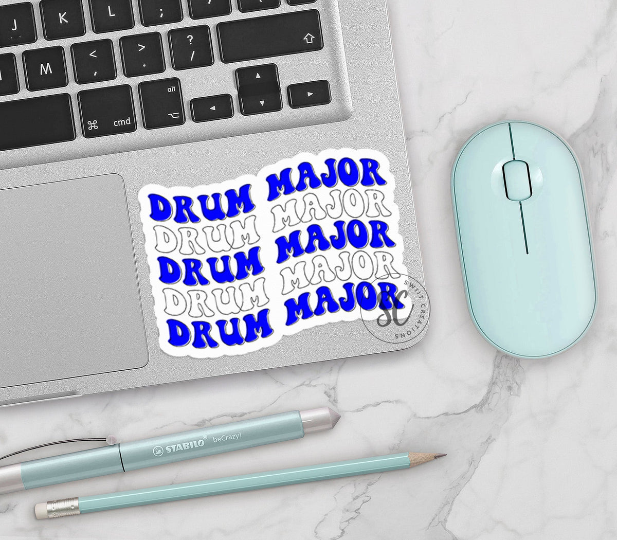 Blue and White Drum Major vinyl sticker on a silver laptop next to a mint mouse and pens
