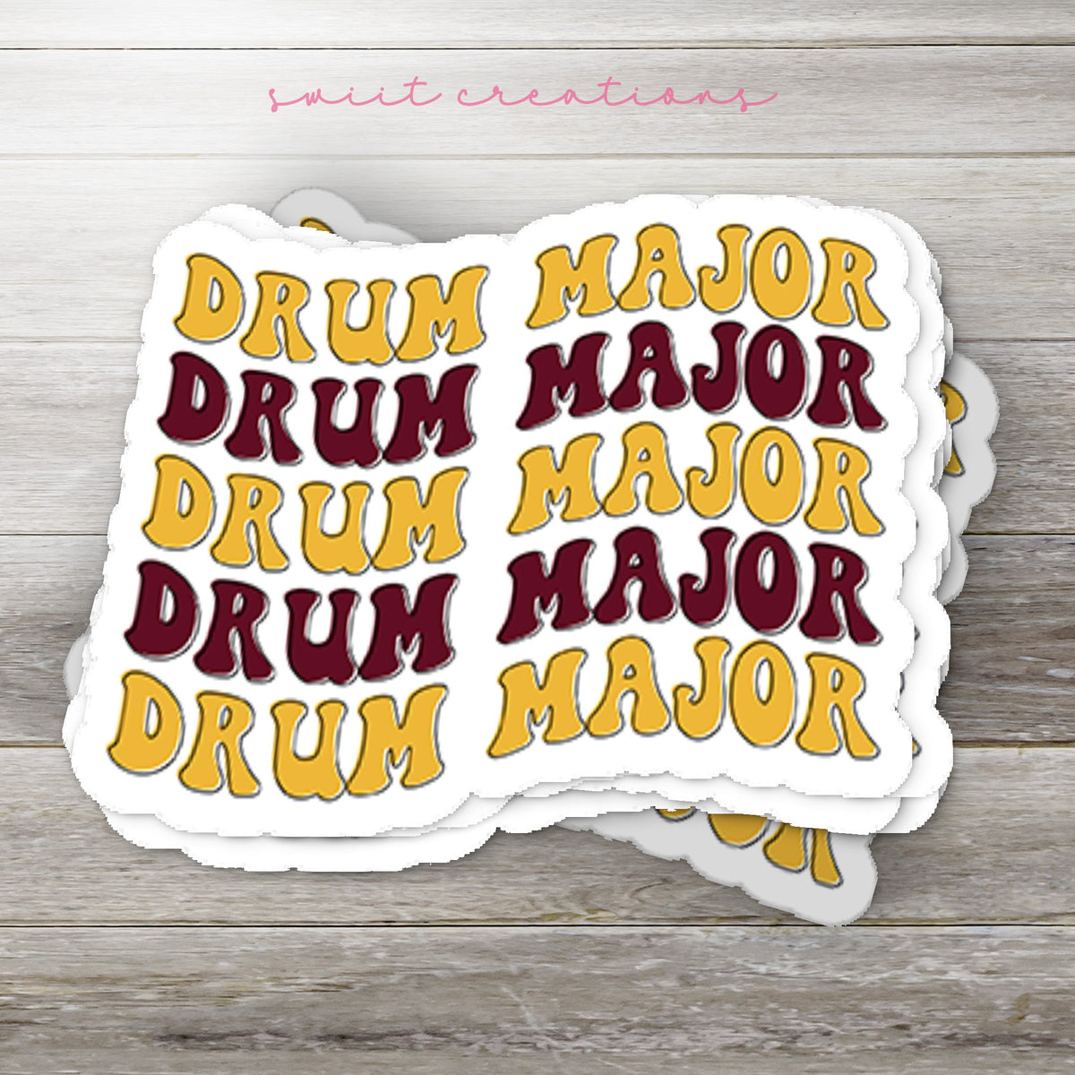 Stack of Maroon and Gold Drum Major glossy stickers on a gray wood table