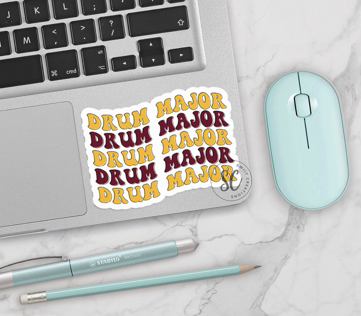 Maroon and Gold Drum Major vinyl sticker on a silver laptop next to a mint mouse and pens