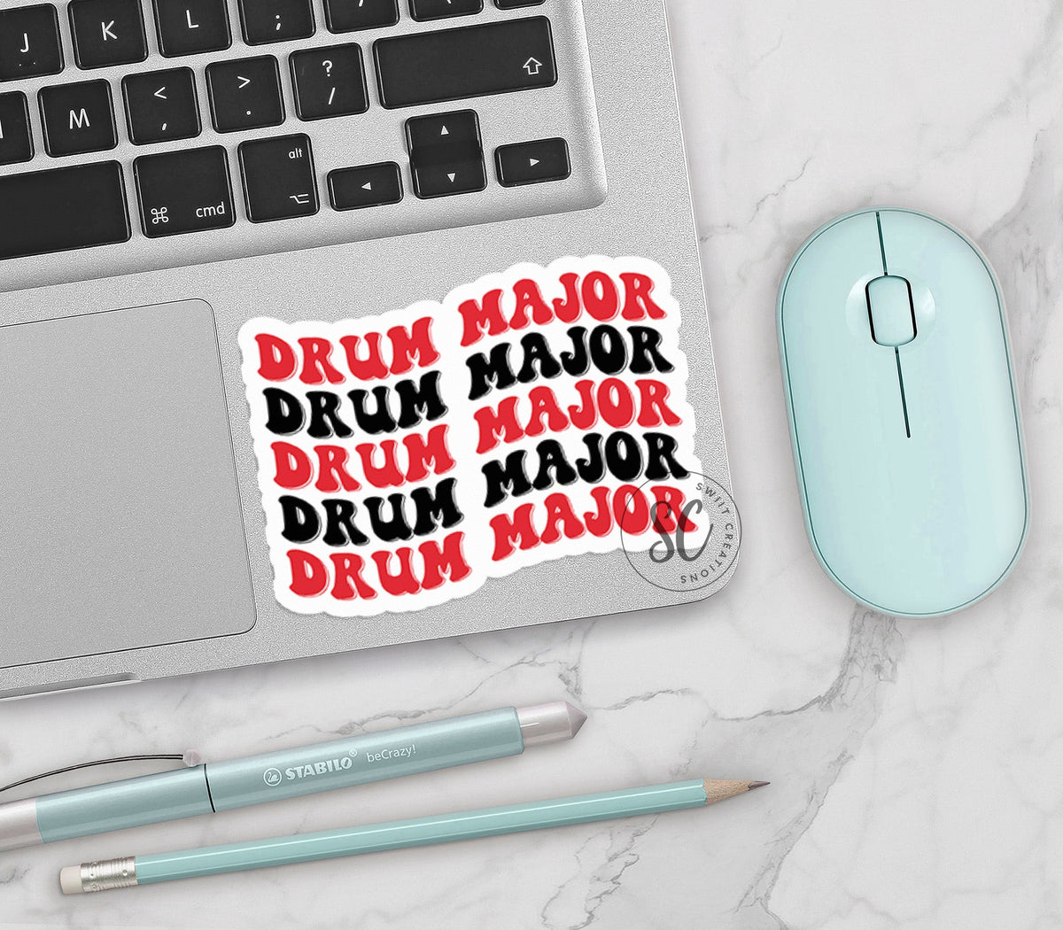 Red and Black Drum Major vinyl sticker on a silver laptop next to a mint mouse and pens