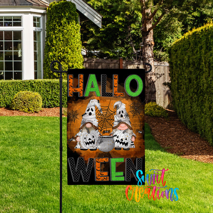 A Halloween-themed garden sign with the text "HALLO WEN" and illustrations of two ghostly gnomes with carved pumpkins.