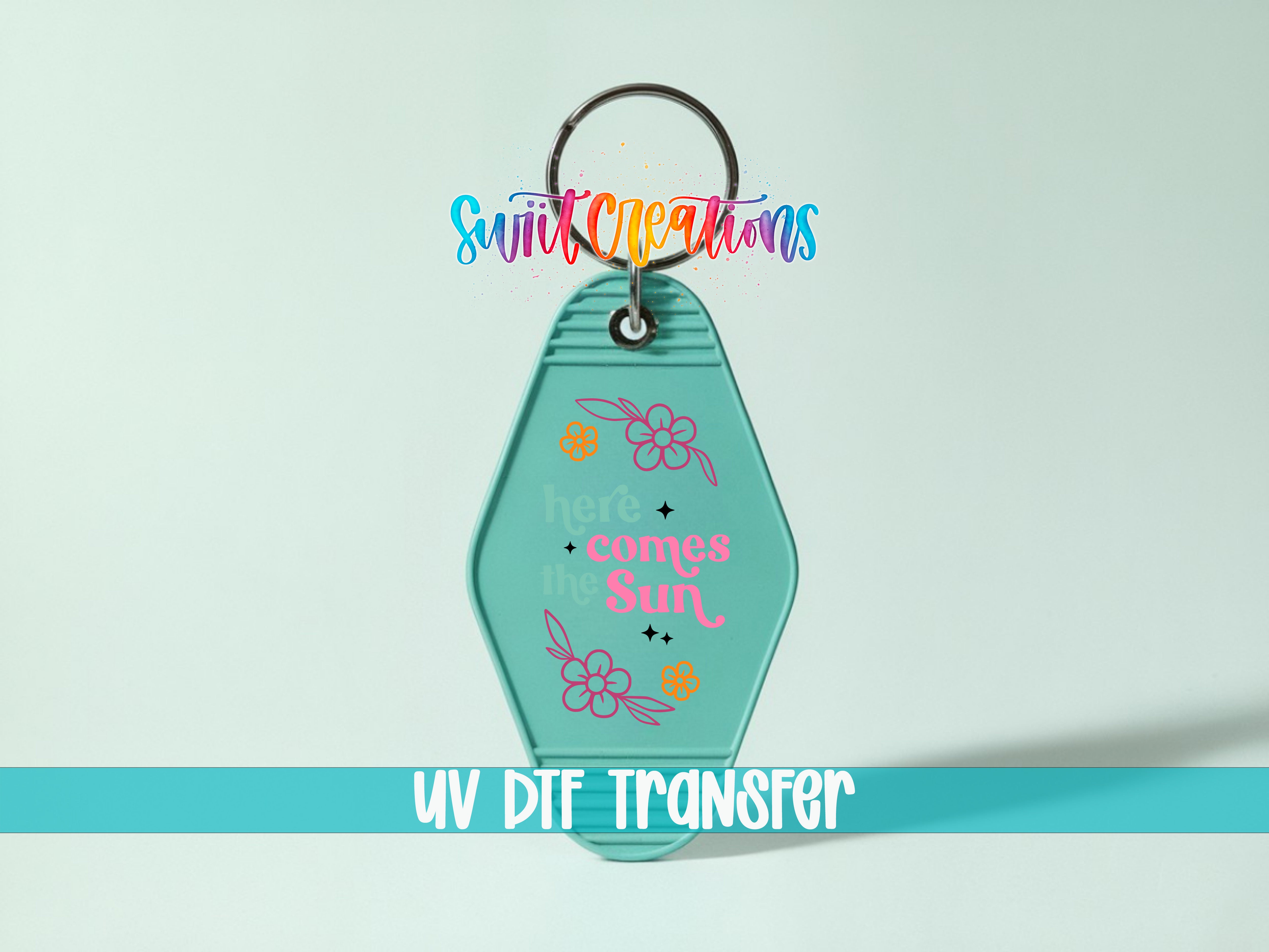 A keychain with a colorful design and text, including the phrase "here comes the sun".