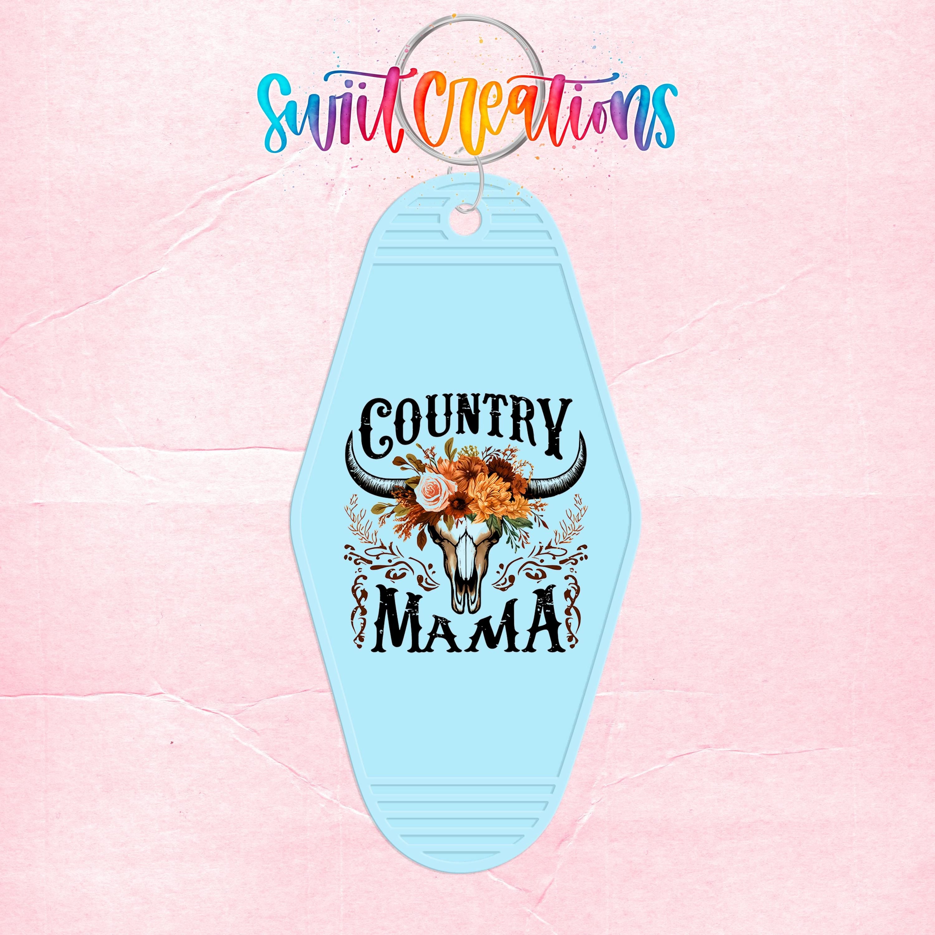 A blue keychain with a decorative design featuring a skull and floral elements, along with the text "Country Mama".