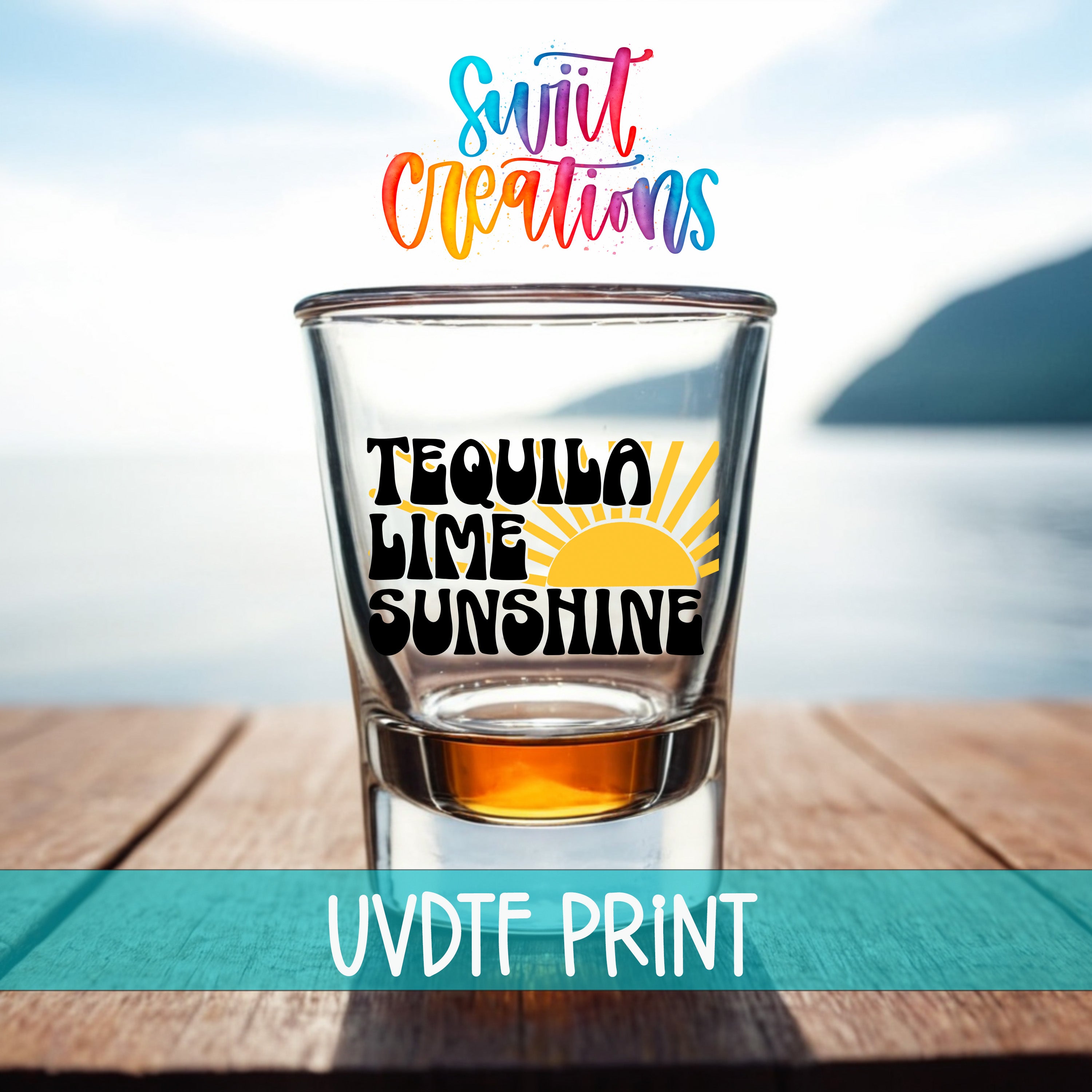 A shot glass with the text "Tequila Lime Sunshine" printed on it, placed on a wooden surface with a scenic background of a body of water and a mountain.