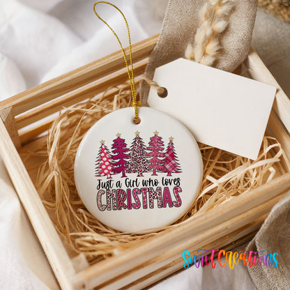 A white ceramic ornament with a Christmas tree design and the text "Just a Girl who loves Christmas" is displayed in a wooden crate.
