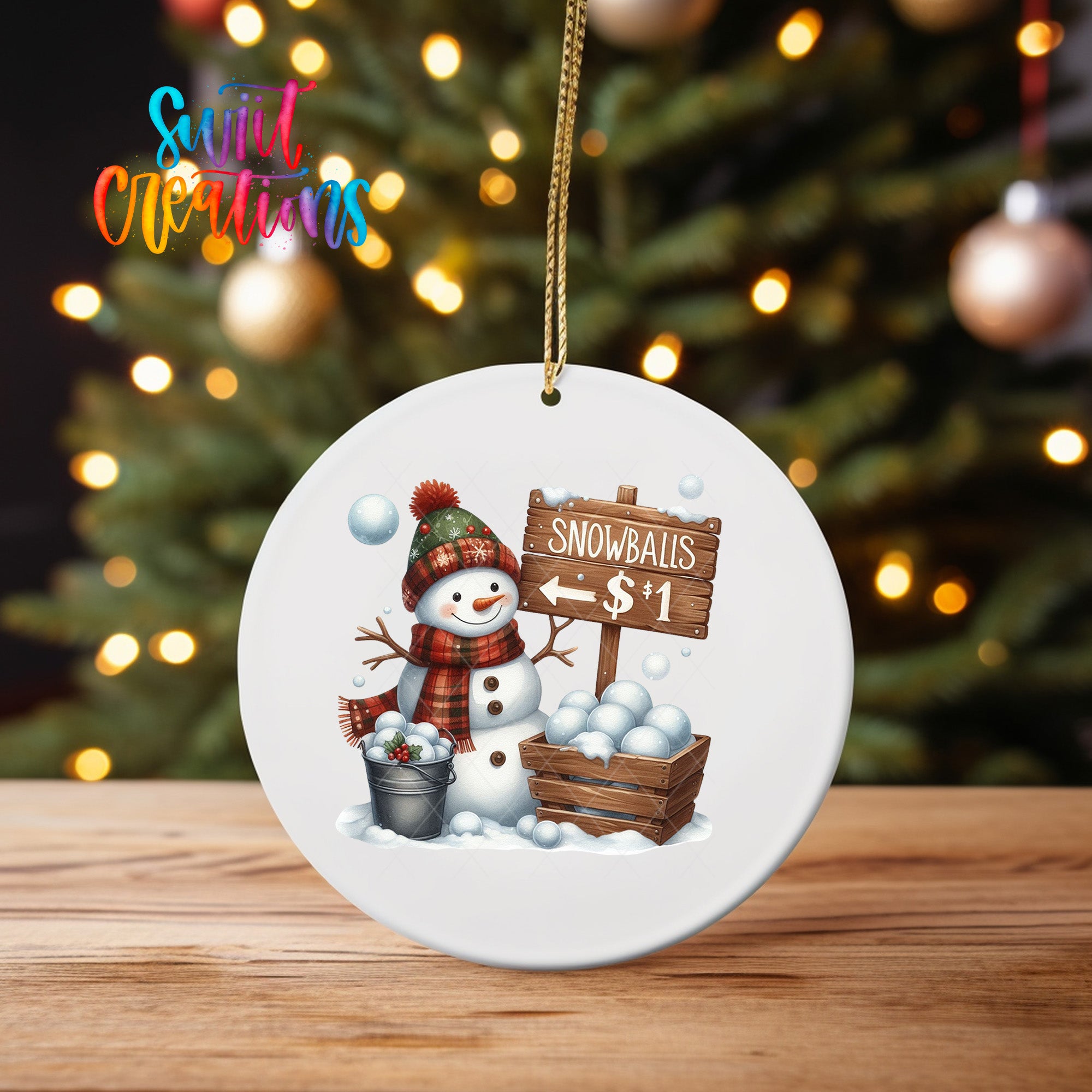 A snowman ornament with a sign that says "Snowballs $1" is displayed on a wooden surface, with a blurred background of a Christmas tree and twinkling lights.