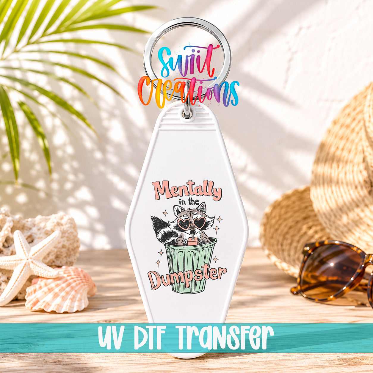 A keychain with a raccoon wearing sunglasses and the text "Mentally in the Dumpster" printed on it, along with a colorful ring and a straw hat.