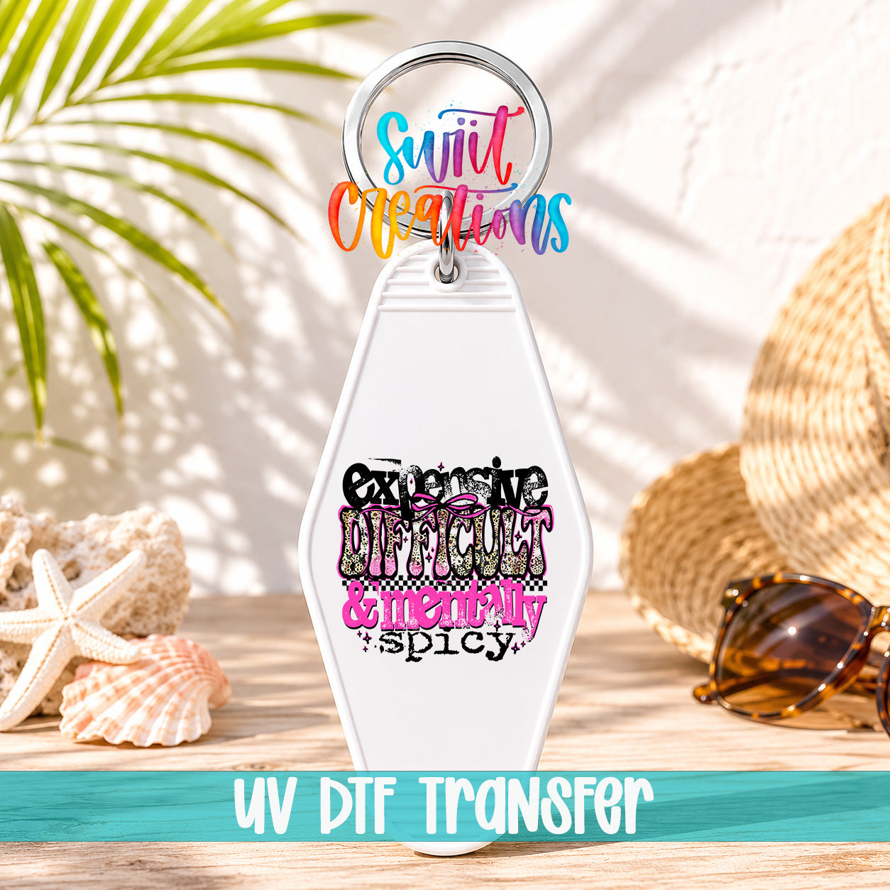 A keychain with a colorful design and text, placed on a wooden surface with sunglasses and a straw hat in the background.