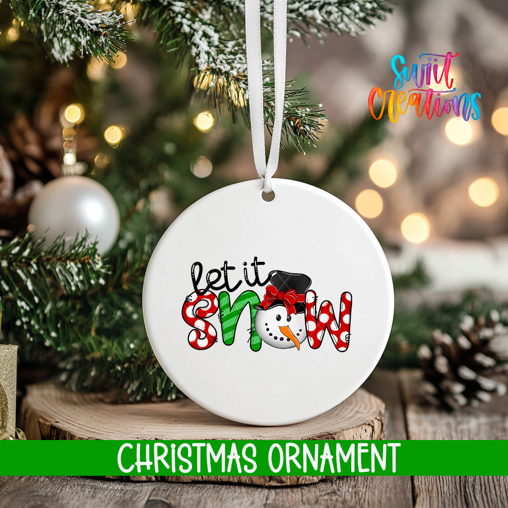 A white Christmas ornament with the text "let it snow" is hanging on a tree branch, surrounded by pine cones and other holiday decorations.