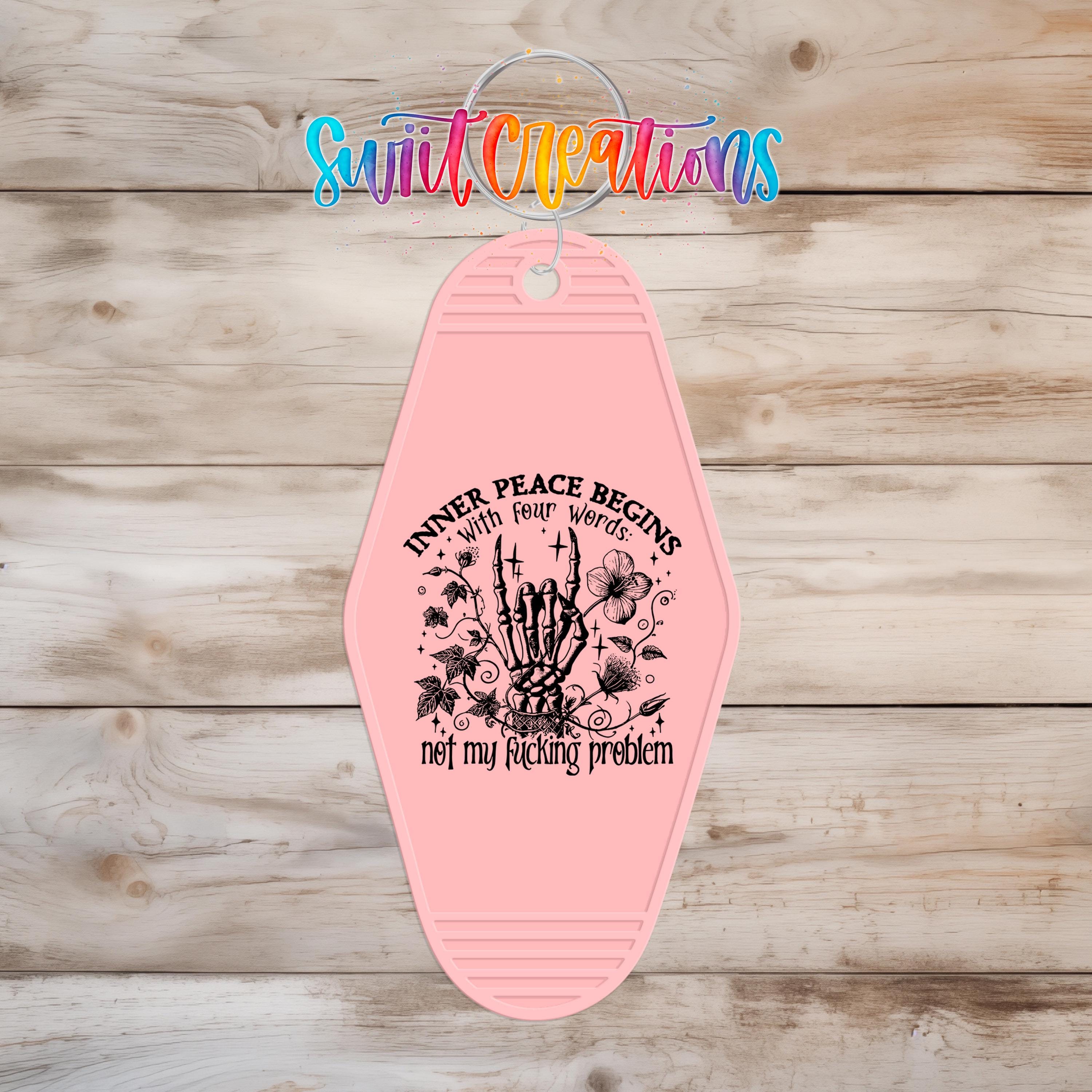 A pink keychain with a graphic design and text on it, hanging on a wooden surface.