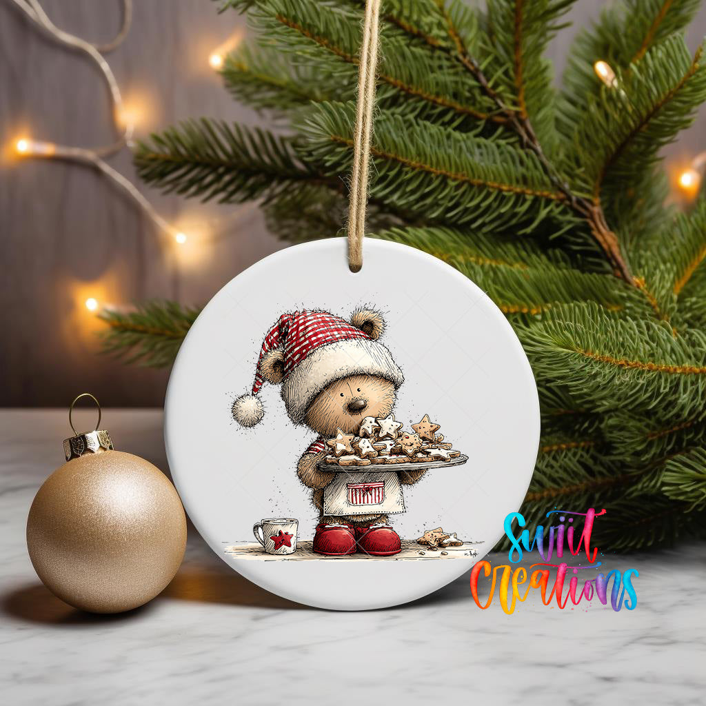A white ceramic ornament featuring a teddy bear wearing a Santa hat and holding a tray of cookies, with a Christmas tree and twinkling lights in the background.