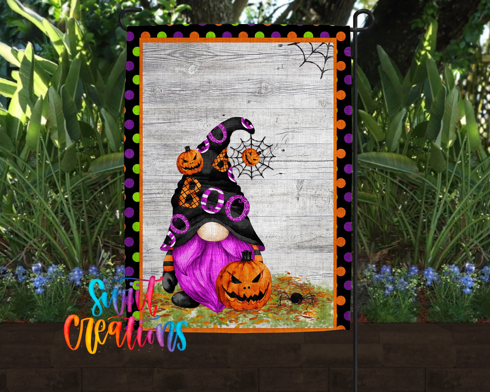 A Halloween-themed garden decoration featuring a gnome with a pumpkin hat and a spider web, surrounded by greenery and flowers.