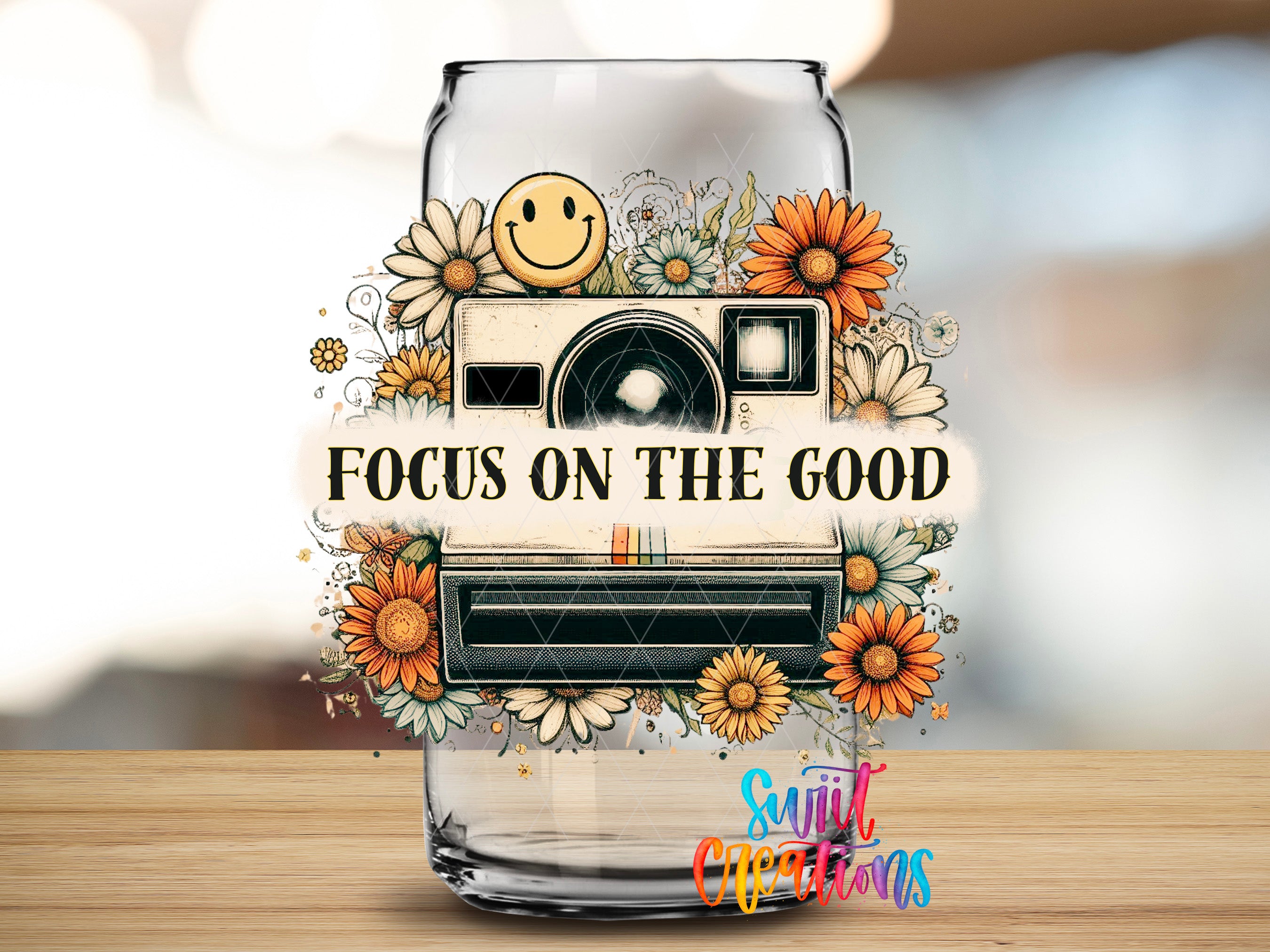a glass jar with a camera and flowers, along with the text "Focus on the good" written on it.