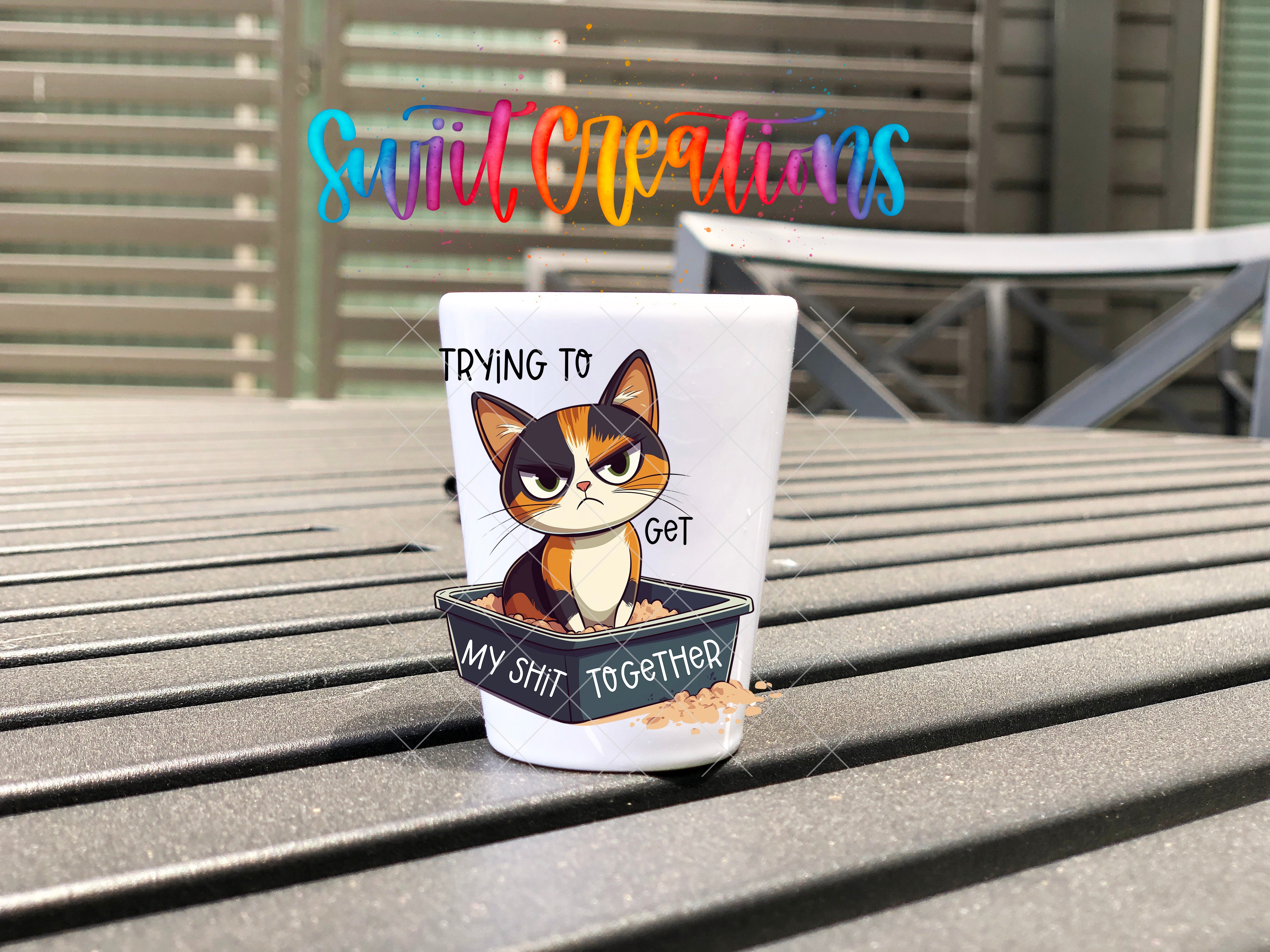 A cup with a cartoon cat illustration and text, sitting on a wooden surface.